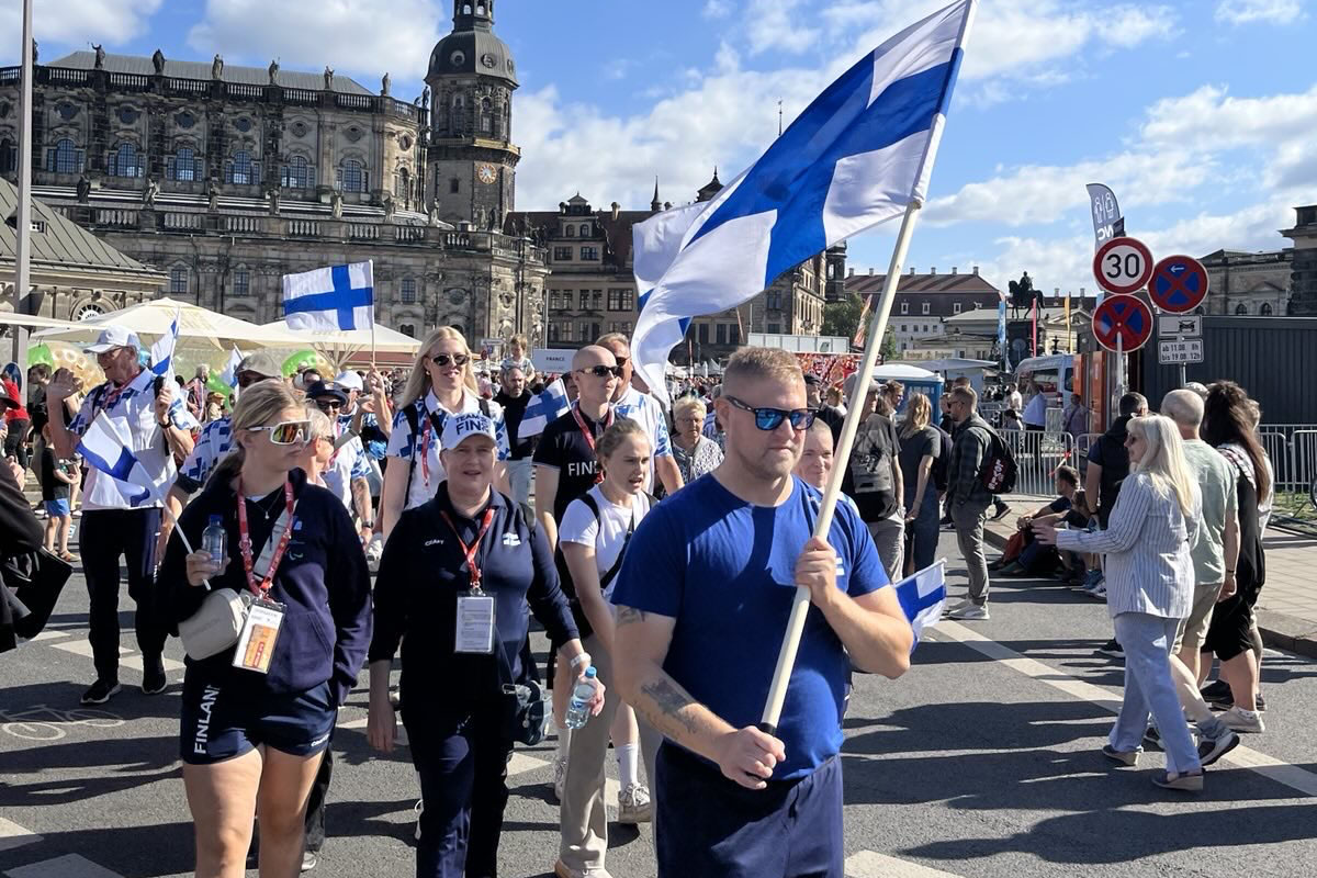 Suomen joukkue marssii avajaiskulkueessa aurinkoisessa Dresdenin vanhassa kaupungissa lippuja heilutellen. Etualalla lipunkantaja Mikael Kock.